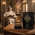 Maison Alhambra Infini Oud Joyous — A man in traditional attire reads a book while smoke rises from a perfume bottle on a wooden table. | Maison Alhambra Infini Oud Joyous — Seorang lelaki berpakaian tradisional membaca buku sementara asap naik dari botol minyak wangi di atas meja kayu.