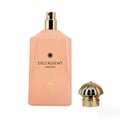Maison Alhambra Decadent Dream — A peach-colored perfume bottle with a gold spray nozzle and cap, standing next to its detached ornate gold cap. | Maison Alhambra Decadent Dream — Botol pewangi berwarna pic dengan muncung semburan dan penutup emas, berdiri di sebelah penutup emasnya yang berhias.