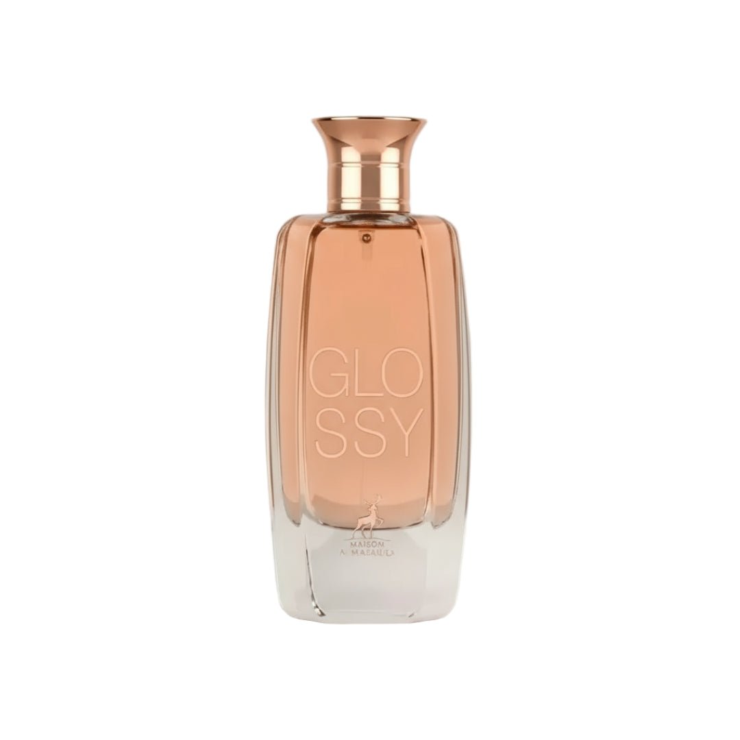 Maison Alhambra Glossy By Maison Alhambra 100ml Women EDP — A clear glass perfume bottle with a rose gold cap and a peach-colored liquid inside, featuring the word "GLOSSY" embossed vertically on the front. | Maison Alhambra Glossy By Maison Alhambra 100ml Women EDP — Botol minyak wangi kaca jernih dengan penutup emas