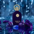 Maison Alhambra Philos Centro Maison Alhambra 100ml EDP — A dark purple velvet perfume bottle with a gold cap and emblem sits in water, surrounded by purple rose petals and blue accents, with a bokeh background of blue lights. | Maison Alhambra Philos Centro Maison Alhambra 100ml EDP — Botol minyak wangi baldu ungu