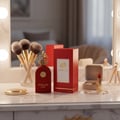 Maison Alhambra Philos Rosso Maison Alhambra 100ml EDP — Red perfume bottle and box with gold accents, makeup brushes in a glass, lipstick, and a compact on a marble vanity | Maison Alhambra Philos Rosso Maison Alhambra 100ml EDP — Botol dan kotak minyak wangi merah dengan aksen emas, berus solek dalam gelas, gincu