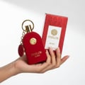Maison Alhambra Philos Rosso — A hand holds a red, velvet-textured perfume bottle with a gold cap and emblem, next to its red patterned box. | Maison Alhambra Philos Rosso — Tangan memegang botol minyak wangi merah bertekstur baldu dengan penutup dan lambang emas, bersebelahan dengan kotaknya yang bermotif merah.