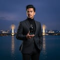 Maison Alhambra Glacier Bold by Maison Alhambra 100ml EDP — Man in a dark suit holding a perfume bottle in front of a city bridge at dusk. | Maison Alhambra Glacier Bold by Maison Alhambra 100ml EDP — Lelaki berbaju gelap memegang botol minyak wangi di hadapan jambatan bandar ketika senja.
