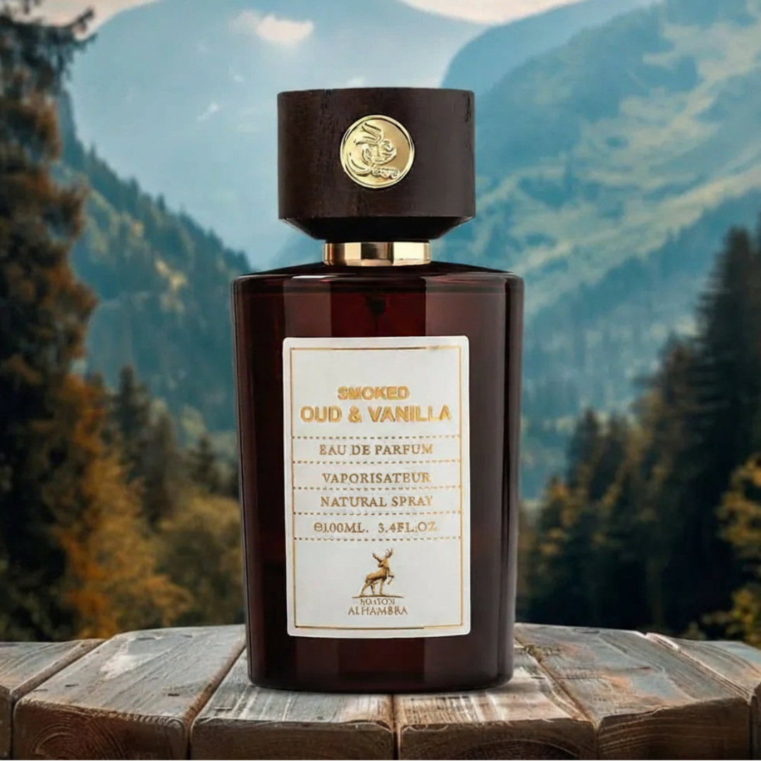 Maison Alhambra Smoked Oud & Vanilla by Maison Alhambra 100ml EDP — A dark brown glass perfume bottle with a wooden cap sits on a rustic wooden table against a blurred background of green mountains and trees. | Maison Alhambra Smoked Oud & Vanilla by Maison Alhambra 100ml EDP — Botol kaca berwarna coklat gelap dengan