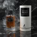 Maison Alhambra Smoky — A glass perfume bottle with amber liquid and a black cap sits on a black marble surface, surrounded by wisps of smoke, next to its cylindrical packaging. | Maison Alhambra Smoky — Botol minyak wangi kaca berisi cecair ambar dan penutup hitam terletak di atas permukaan marmar hitam, dikelilingi