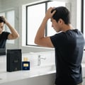 Maison Alhambra Spectrum by Maison Alhambra 100ml EDP Men — Man styling hair in front of a bathroom mirror with the perfume bottle and box on the counter. | Maison Alhambra Spectrum by Maison Alhambra 100ml EDP Men — Lelaki menggayakan rambut di hadapan cermin bilik mandi dengan botol dan kotak minyak wangi di atas