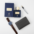 Maison Alhambra Spectrum by Maison Alhambra 100ml EDP Men — A dark blue perfume bottle and its matching box sit next to a dark grey wallet, a brown leather watch, and a silver fountain pen on a white background. | Maison Alhambra Spectrum by Maison Alhambra 100ml EDP Men — Botol minyak wangi biru gelap dan kotaknya