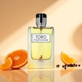 Maison Alhambra Toro Pour Homme – A clear glass bottle of yellow liquid perfume with a silver cap, placed on a reflective surface with sliced oranges and peppercorns. | Maison Alhambra Toro Pour Homme – Botol kaca jernih berisi minyak wangi kuning dengan penutup perak, diletakkan di permukaan reflektif bersama hirisan