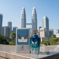 Maison Alhambra Victorioso Legend — A blue glass perfume bottle and its box stand on a stone surface with the Petronas Twin Towers in the background. | Maison Alhambra Victorioso Legend — Botol kaca biru pewangi dan kotaknya berdiri di atas permukaan batu dengan latar belakang Menara Berkembar Petronas.