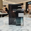 Maison Alhambra Yeah by Maison Alhambra 100ml EDP Men — A black perfume box and bottle are displayed on a marble surface in a mall setting. | Maison Alhambra Yeah by Maison Alhambra 100ml EDP Men — Kotak dan botol minyak wangi hitam dipamerkan di atas permukaan marmar dalam suasana pusat beli-belah.