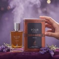 Maison Alhambra Your Touch Intense by Maison Alhambra 100ml — A glass perfume bottle with amber liquid and a silver cap stands next to its copper and black box, with lavender sprigs and purple fabric in the foreground, and a smoky, bokeh background. | Maison Alhambra Your Touch Intense by Maison Alhambra 100ml —